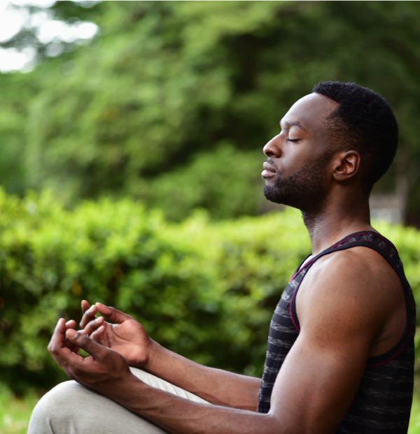 A young man sitting on the ground at a park, meditating.