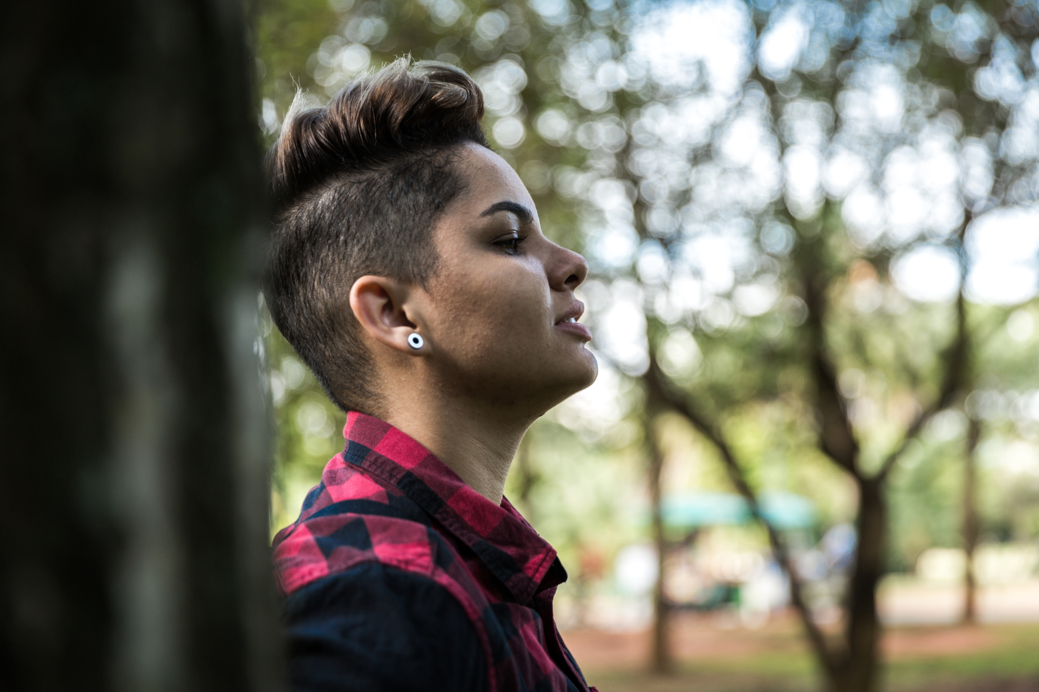 Close up portrait of a young person leaning up against a fence. They have a short, trendy haircut and prominent earrings.