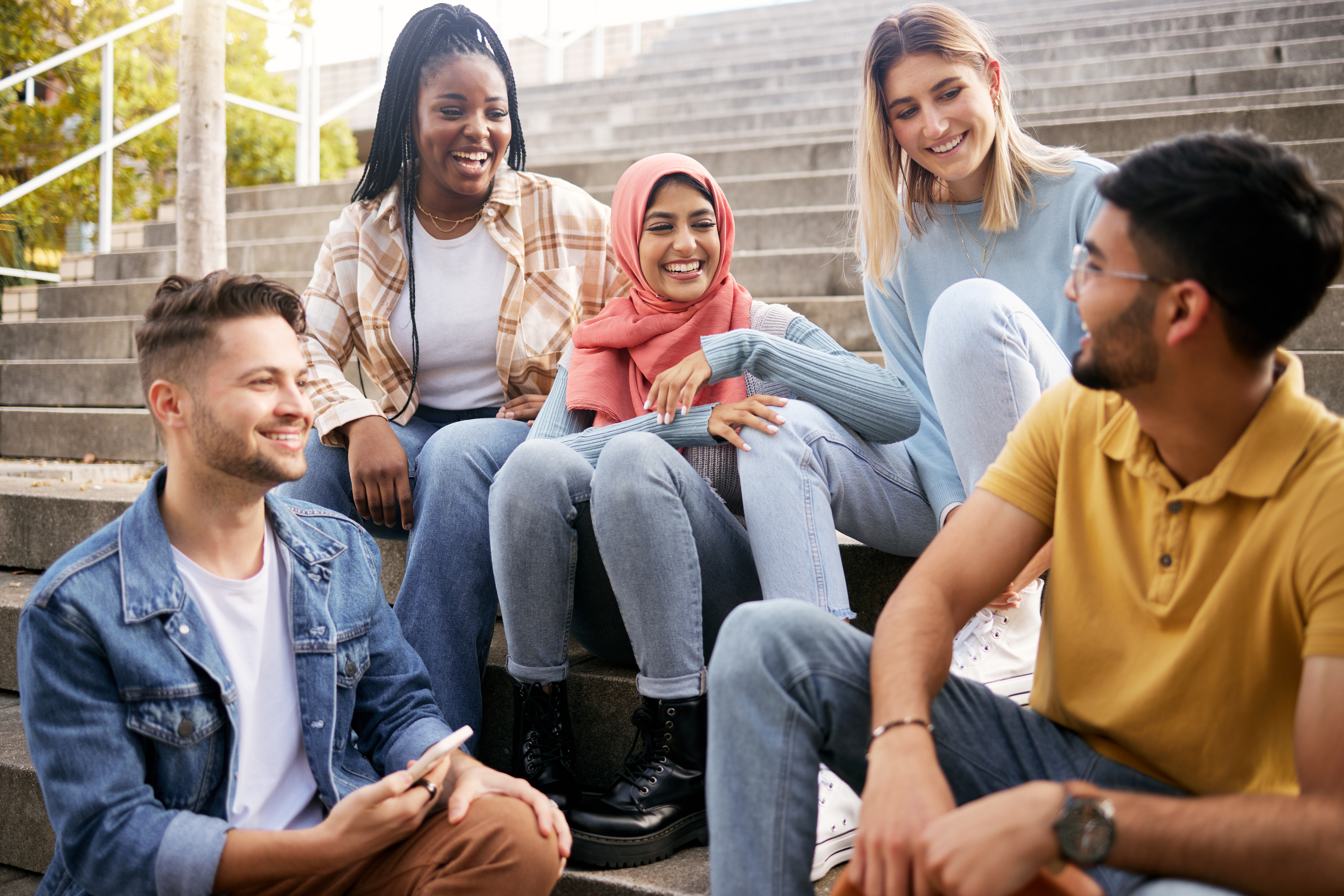 group of five young adults sitting on steps outdoors and talking